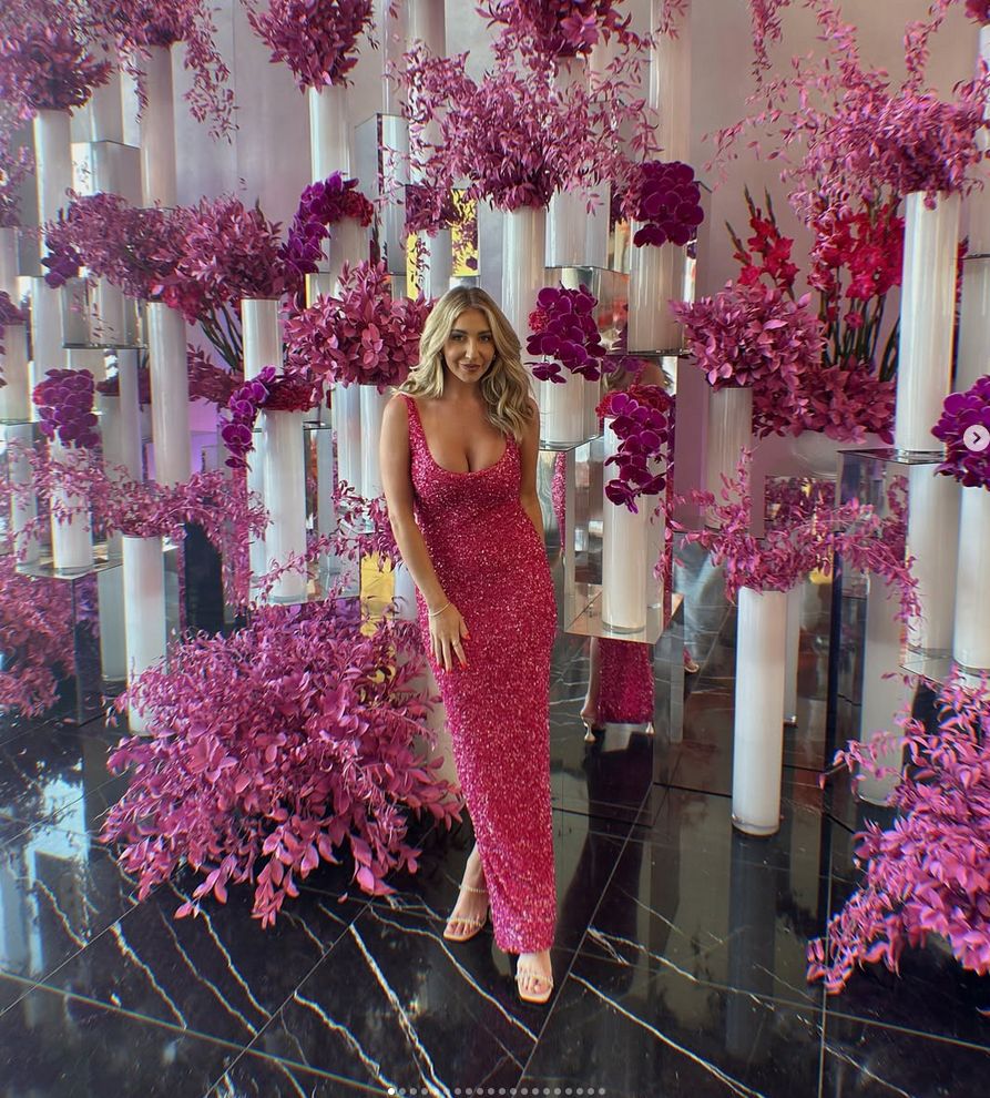 Alicia smiling in front of a wall of pink flowers